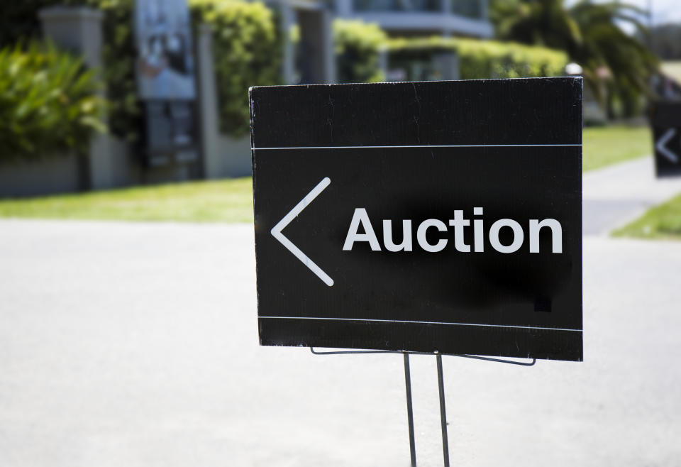 Auction sign, outside suburban house, positioned on front lawn.