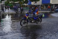 A man rides his motorcycle over a puddle in Caracas, Venezuela, Wednesday, June 29, 2022. As the latest tropical disturbance advances through the area, Venezuela shuttered schools, opened shelters and restricted air and water transportation on Wednesday as President Nicolas Maduro noted that the South American country already has been struggling with recent heavy rains. (AP Photo/Ariana Cubillos)