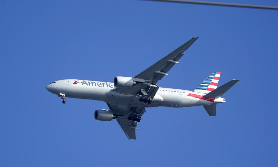 An American Airlines Boeing 777 is framed by utility wires as it prepares to land at Miami International Airport, Wednesday, Jan. 27, 2021, in Miami. The airline said Thursday that it lost $2.2 billion in the fourth quarter, with revenue plunging by nearly two-thirds from a year earlier. And the airline lost $8.9 billion for the full year after earning nearly $1.7 billion in 2019. .(AP Photo/Wilfredo Lee)