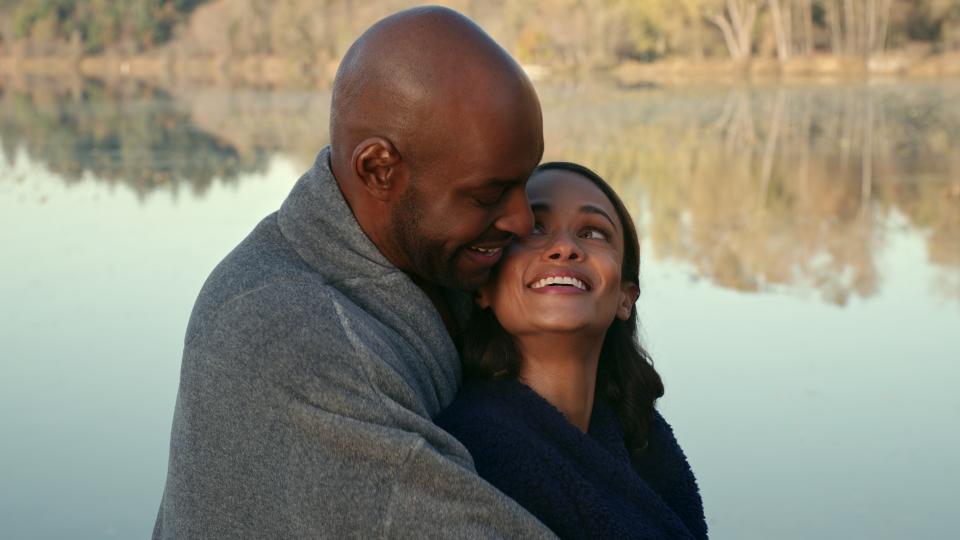 Preacher hugs Kaia from behind as she looks up at him smiling.