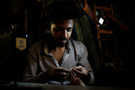 A tailor works under the light of a mobile phone torch, during power outage, at his shop in Karachi, Pakistan April 12, 2018. REUTERS/Akhtar Soomro/Files