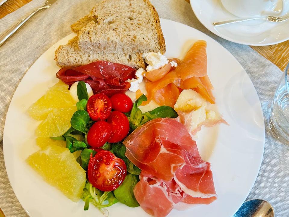 A white plate filled with various meats, a salad with bright-red tomatoes, yellow citrus fruits, and a piece of bread