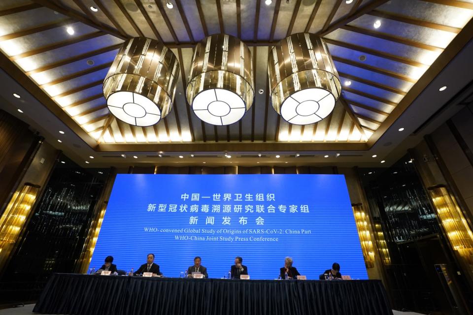 People in suits sit at a table in front of a large blue screen that has Chinese characters English words.