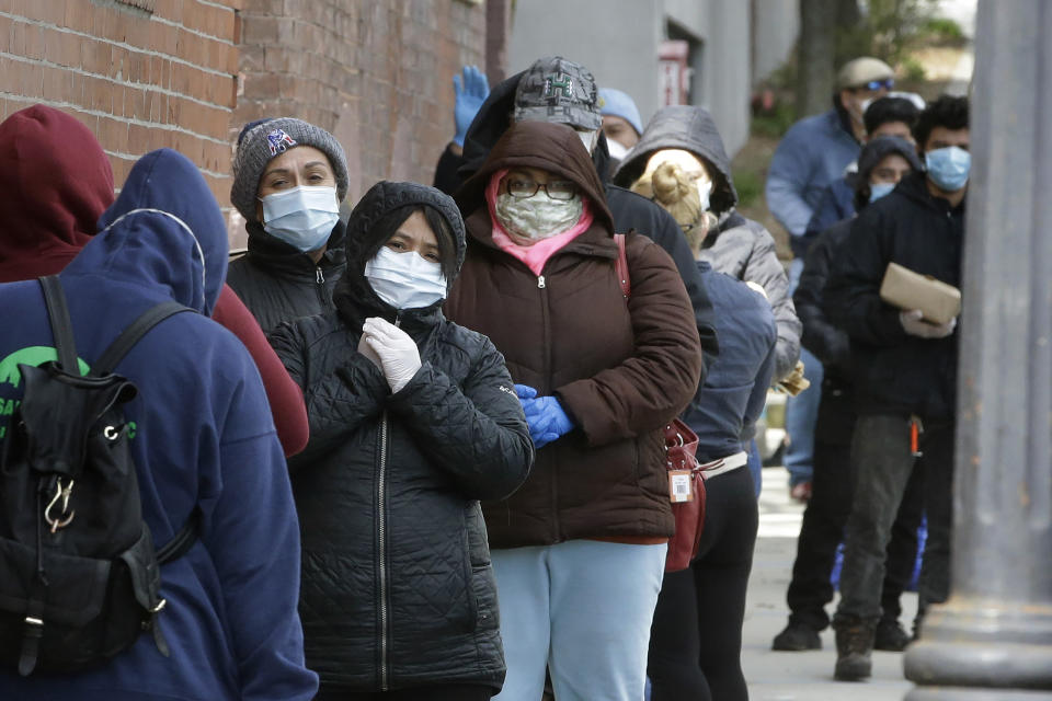 People wear protective masks out of concern for the coronavirus while standing in line outside a pop-up food pantry, Thursday, April 16, 2020, in Chelsea, Mass. (AP Photo/Steven Senne)