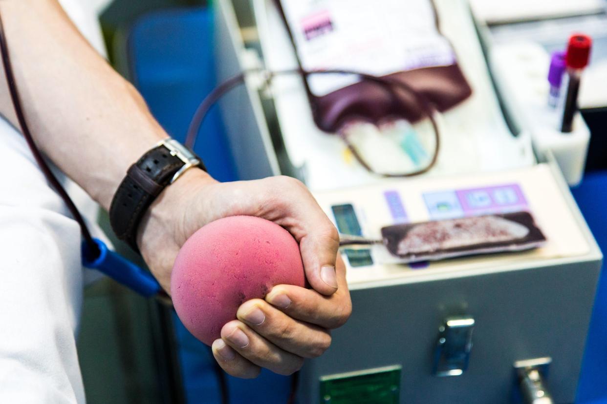 Color image depicting a blood donor in the process of donating blood in a medical clinic. Focus on the donor's arm and they are squeezing a foam ball to help the blood flow quicker. Room for copy space.