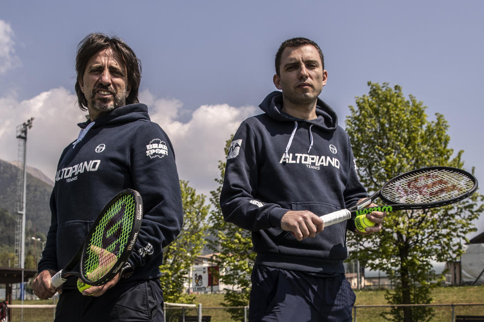 In this image take on Friday, April 24, 2020 Italian Tennis Federation coaches Daniele Brasi, 41, right, is flanked by his brother Luca Brasi, 55, as they pose for a portrait on their tennis court in Rovetta, near Bergamo, northern Italy. The brothers, who lost an uncle to COVID-19, run one of the biggest Italian Tennis Federation centers in the valley. They rely on tourism for about 50% of their yearly income, the rest comes from roughly 900 school students who follow courses throughout the winter, including some 20 under-18 professionals. (AP Photo/Luca Bruno)