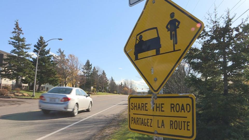Active travel such as walking, biking and carpooling, is part of the government's transportation action plan. (Brian Higgins/CBC) A Charlottetown road is pictured with a traffic sign indicating to "Share the Road." A car is seen driving away, next to a separated bike lane. 