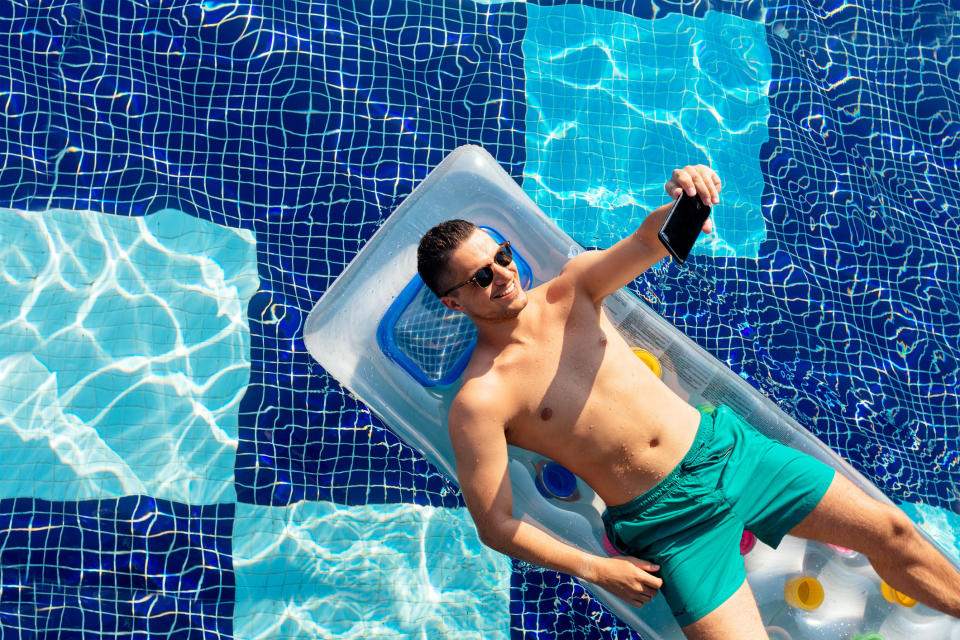 Smiling man lying on a floatie in a pool and taking a selfie