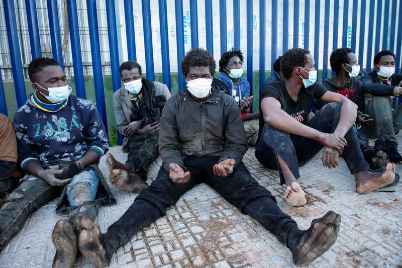 Migrants sit outside the temporary migrants center upon crossing the border fence, in Melilla