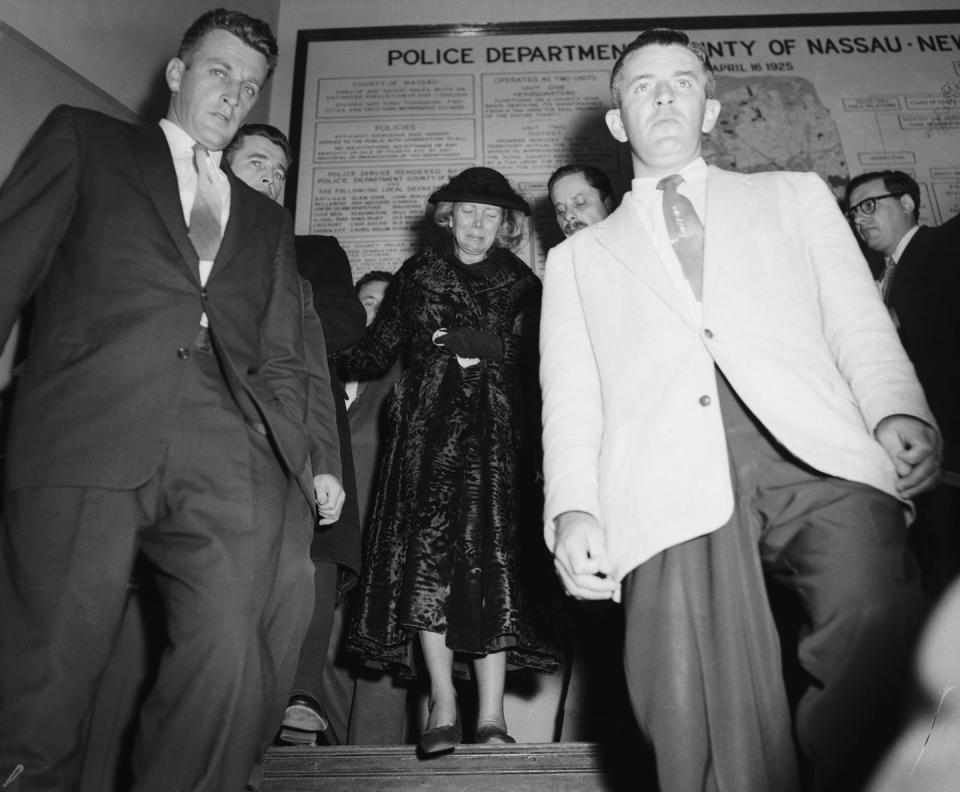 ann woodward cries while walking down a staircase with several other people, she wears a long dark coat, a hat and gloves