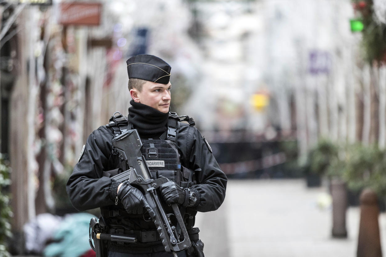 Ein schwer bewaffneter Polizist bewacht die Gegend um den Tatort. (Bild: Jean Francois Badias/AP/dpa)