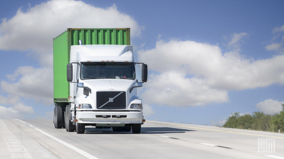 A white tractor hauling a green ocean container