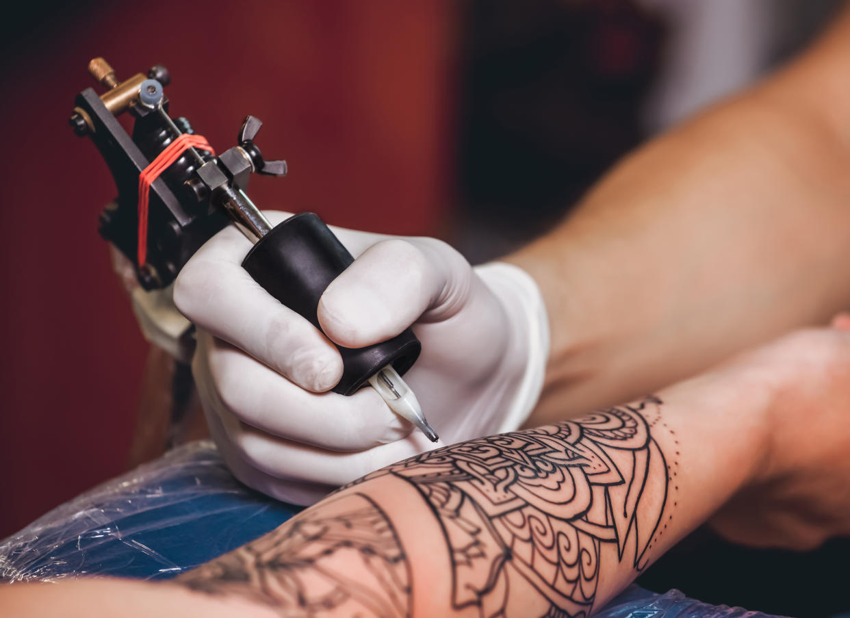 Tattoo master protective gloves make a tattoo in black ink on the hand of the girl. Close-up.