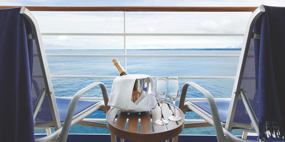 Two lounge chairs on a balcony with a small table holding glasses and a bottle facing the water.