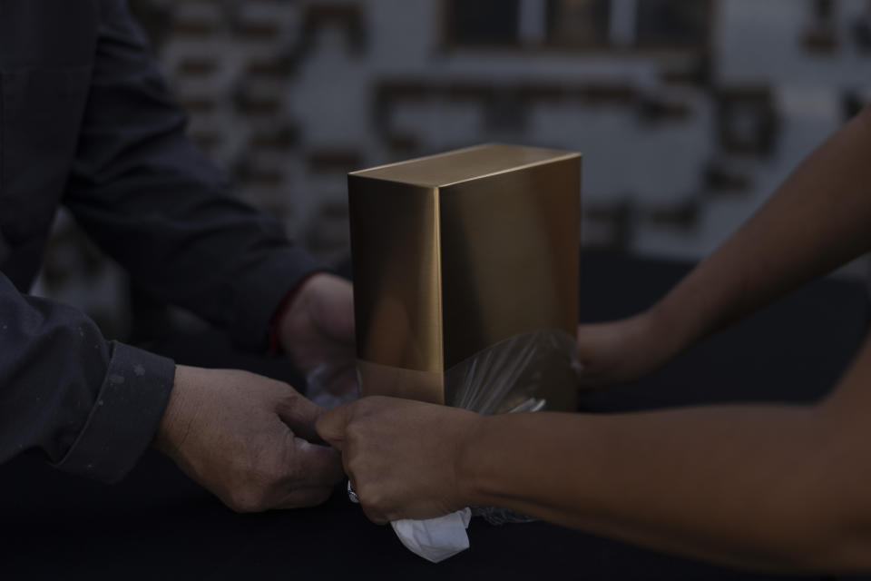 Cemetery worker Jorge Alberto Cortez, on the left, and manager Yuri Hernandez remove the plastic wrap from an urn holding the ashes of an unclaimed Los Angeles County resident as they prepare to place it into a columbarium at Odd Fellows Cemetery in Los Angeles on Thursday, Dec. 14, 2023. (AP Photo/Jae C. Hong)