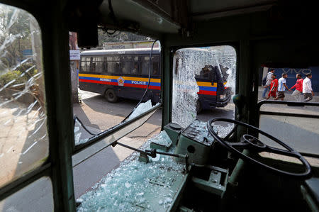 A police van carrying personnel drives past a damaged public bus during a protest in Mumbai, India January 2, 2018. REUTERS/Danish Siddiqui