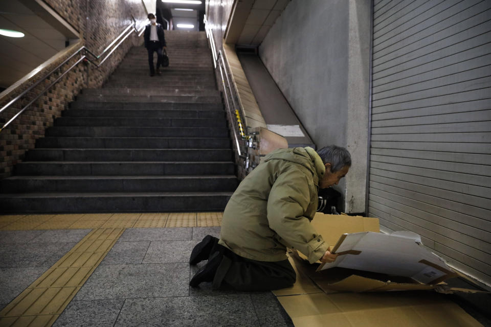 In this Thursday, Jan. 9, 2020, photo, a homeless man lays cardboard to spend the night at Shinjuku Station, in Tokyo. The dozens of homeless people sleeping rough in shuttered Tokyo subway stations worry that with Japan's image at stake authorities will force them to move ahead of the Olympics. (AP Photo/Jae C. Hong)