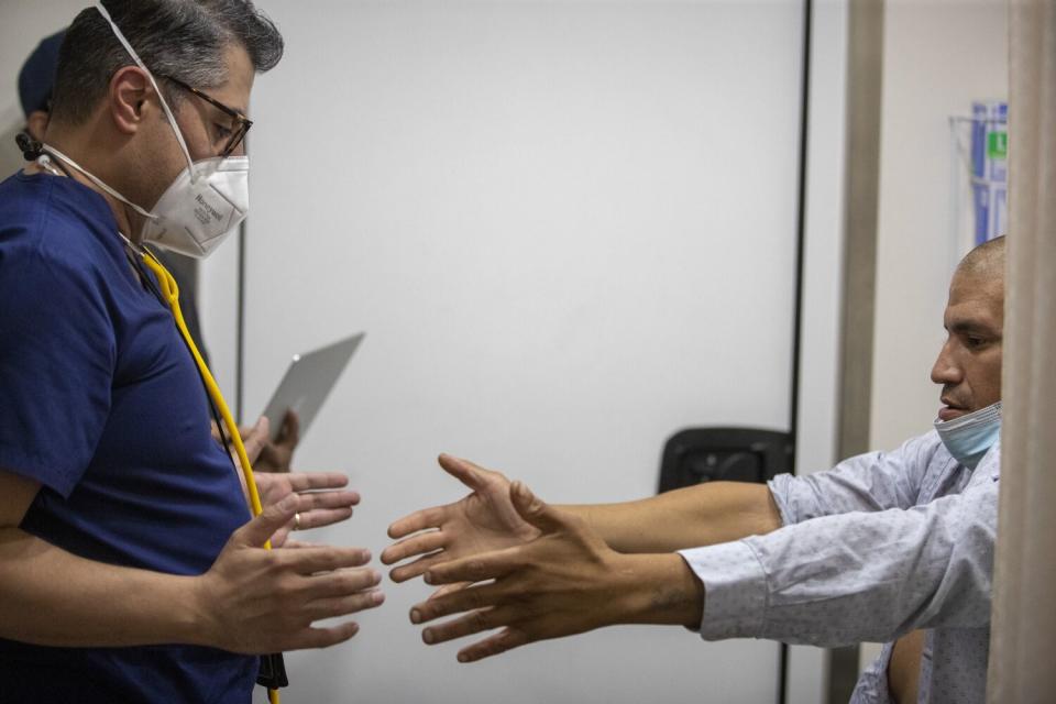 A doctor in scrubs examines a patient with his arms outstretched