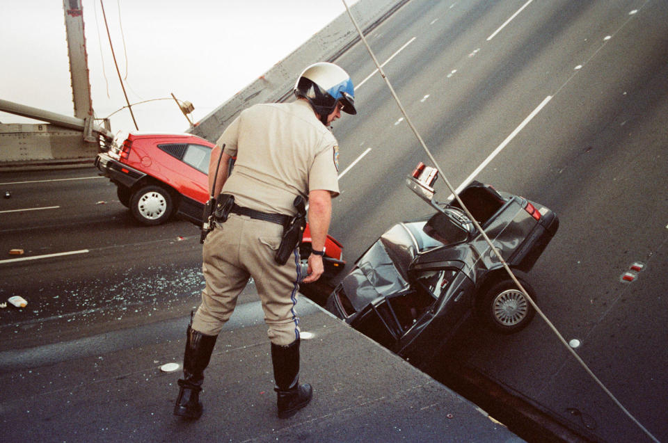 A California Highway Patrol officer checks damage to cars that fell when the upper deck of the Bay Bridge collapsed onto the lower deck following the Loma Prieta earthquake in San Francisco on Oct. 17, 1989. (George Nikitin/AP File)