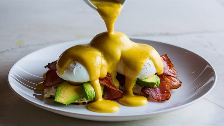 Pouring hollandaise on eggs Benedict