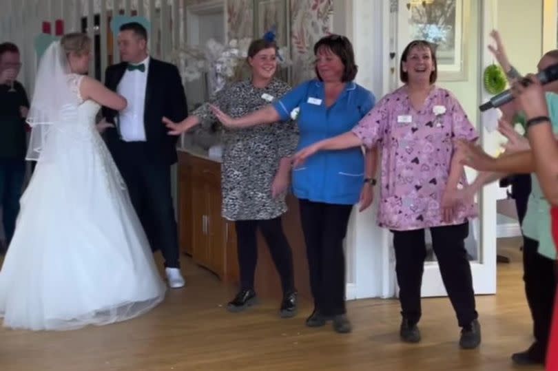 A bride and groom dancing in a care home with elderly residents watching