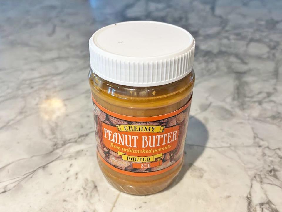 A jar of peanut butter with an orange label depicting illustrations of peanuts with a white lid