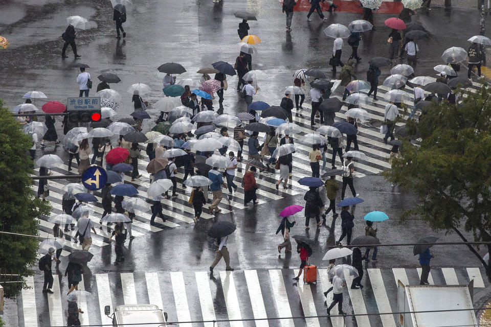 Commuters with umbrellas walk a crosswalk as Typhoon Mindulle travels off the coast of Japan Friday, Oct. 1, 2021, in Tokyo. (AP Photo/Kiichiro Sato)