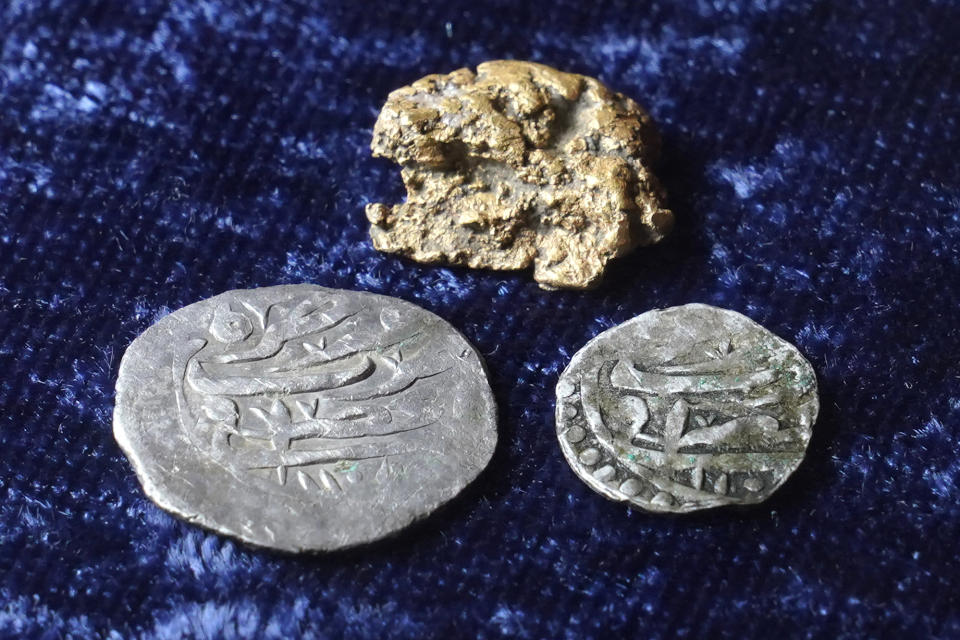 Late 17th century silver coins with Arabic inscriptions, below, and a gold nugget, above, rest on a table in Warwick, R.I., Thursday, Oct. 27, 2022. Metal detectorist Jim Bailey believes the gold nugget, found in a potato field, in Little Compton, R.I., about a mile from where the silver coins were found, likely originated somewhere alongAfrica's Gold Coast, a center for the slave tradein the late 17th and early 18th centuries. (AP Photo/Steven Senne)