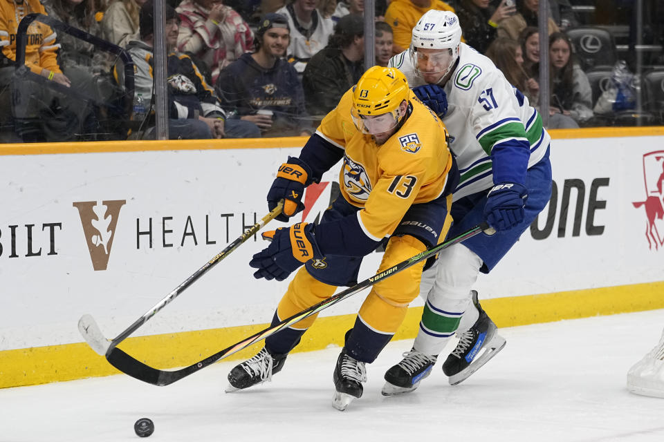 Nashville Predators center Yakov Trenin (13) and Vancouver Canucks defenseman Tyler Myers (57) battle for the puck during the second period of an NHL hockey game Tuesday, Dec. 19, 2023, in Nashville, Tenn. (AP Photo/George Walker IV)