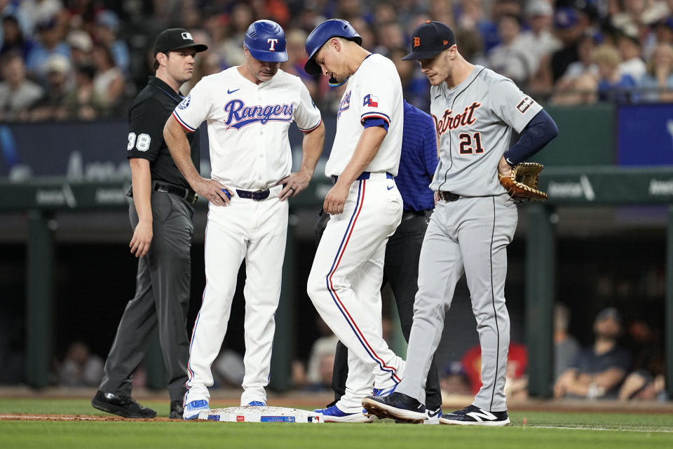 Texas Rangers' Corey Seager, center, right, talks with first base coach Corey Ragsdale, center left, as umpire Adam Beck (38) and Detroit Tigers' Mark Canha (21) stand nearby during the second inning of a baseball game, Wednesday, June 5, 2024, in Arlington, Texas. Seager left the game. (AP Photo/Tony Gutierrez)