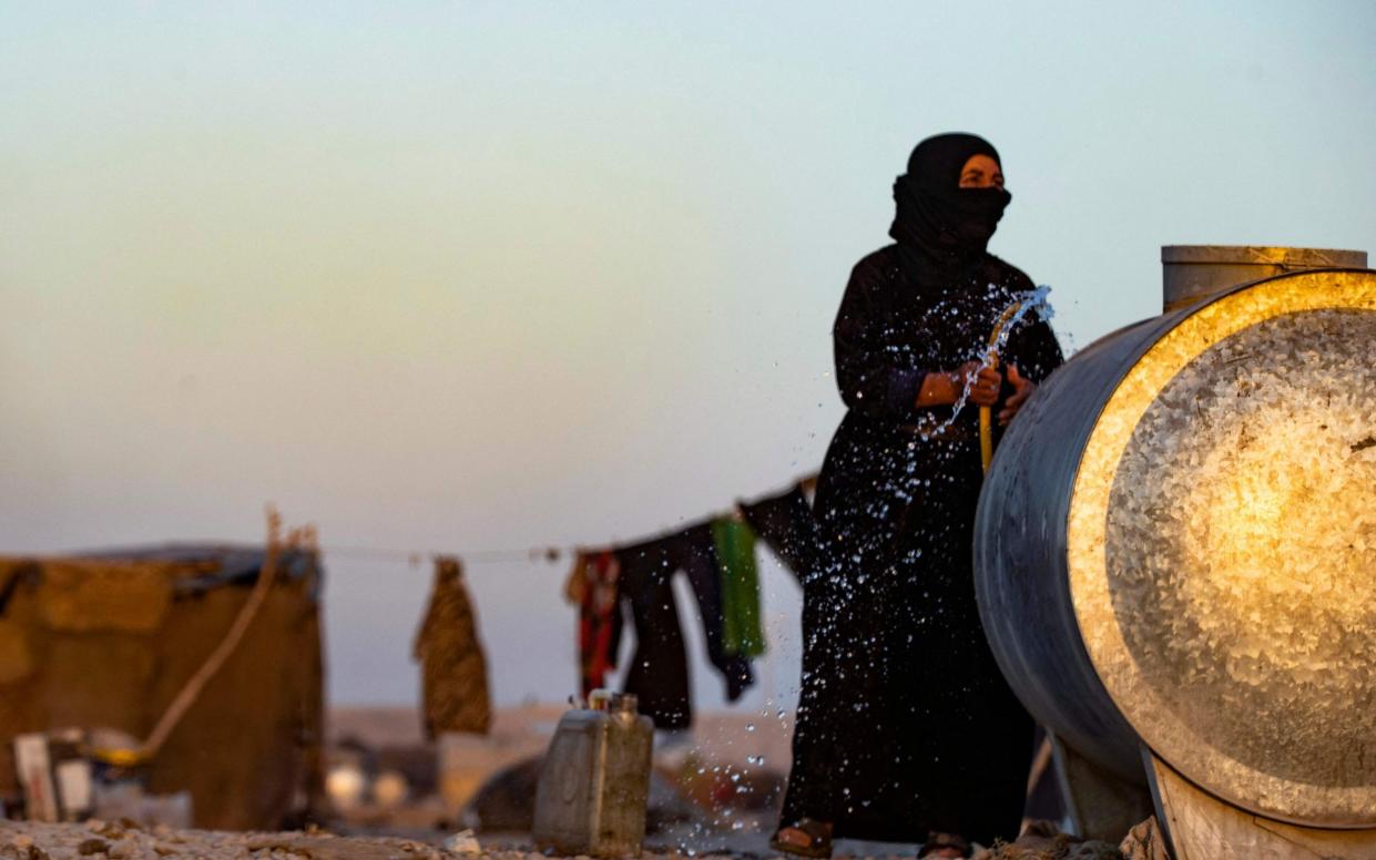 A Syrian woman fills a container with water at the Sahlah al-Banat camp in the countryside of Raqa, in northern Syria - AFP