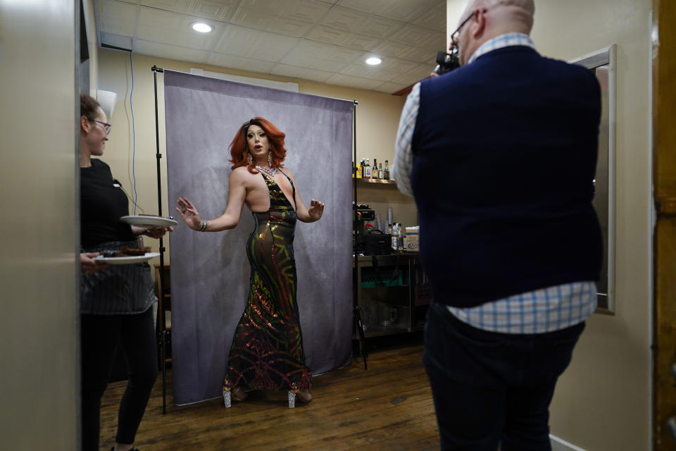 A waitress pauses with plates of food as drag queen Harpy Daniels, aka Joshua Kelley, poses for a photograph taken by Ryan Geiger, right, before the "Daniels Family Values" drag show at the Heritage Restaurant in Shamokin, Pa., Saturday, April 16, 2022. A petty officer first class, Kelley was named a "digital ambassador" by the U.S. Navy to do outreach to the LGBTQ+ community. (AP Photo/Carolyn Kaster)