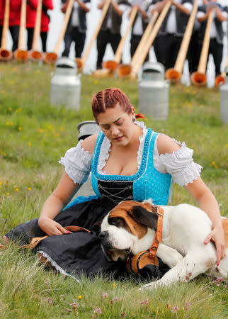 A woman with a dog is seen as alphorn blowers perform an ensemble piece on the last day of the Alphorn International Festival on the alp of Tracouet in Nendaz, southern Switzerland, July 22, 2018. REUTERS/Denis Balibouse