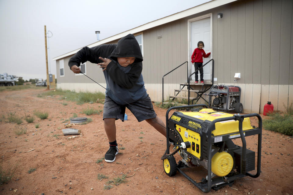 In this Wednesday, May 8, 2019 photo, Jayden Long, 13, starts the generator behind his Kaibeto home on the Navajo Reservation in Arizona, so that he can charge his cell phone inside the family home. An ambitious project to connect homes to the electric grid on the country's largest American Indian reservation is wrapping up. Utility crews from across the U.S. have volunteered their time over the past few weeks to hook up about 300 homes on the Navajo Nation. (AP Photo/Jake Bacon)