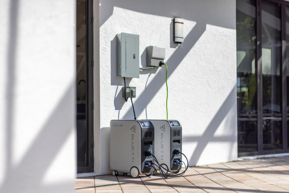 Two models of the BLUETTI Solar Power Station EP500Pro outside of the home connected to electrical box.