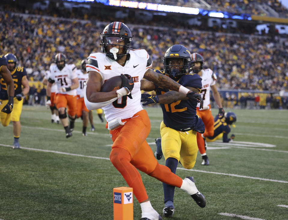 Oklahoma State's Ollie Gordon (0) carries the ball in for a rushing touchdown as West Virginia's Anthony Wilson (12) pursues during the second half of an NCAA college football game Saturday, Oct. 21, 2023, in Morgantown, W.Va. (AP Photo/Chris Jackson)