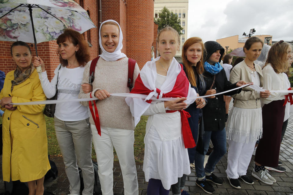 Protesters holding a wait ribbon, a symbol of protest, stand in front of the Church of Saints Simon and Helena during a rally in Minsk, Belarus, Thursday, Aug. 27, 2020. Russian President Vladimir Putin warned that he stands ready to send police to Belarus if protests there turn violent, but added in an interview broadcast Thursday that there is no such need now and voiced hope for stabilizing the situation in the neighboring country. (AP Photo/Dmitri Lovetsky)