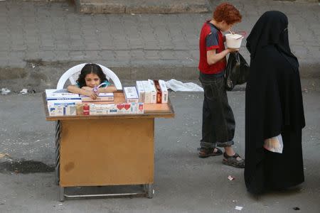 A boy eats yogurt near a girl selling cigarettes in the rebel held al-Shaar neighborhood of Aleppo, Syria, August 30, 2016. REUTERS/Abdalrhman Ismail