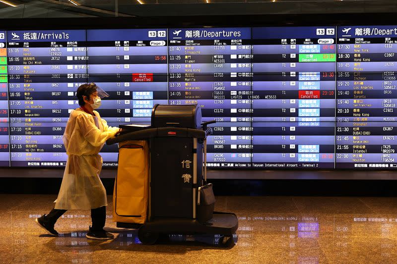 An airport staff walks past a board showing departure statuses at Taoyuan International Airport in Taoyuan City