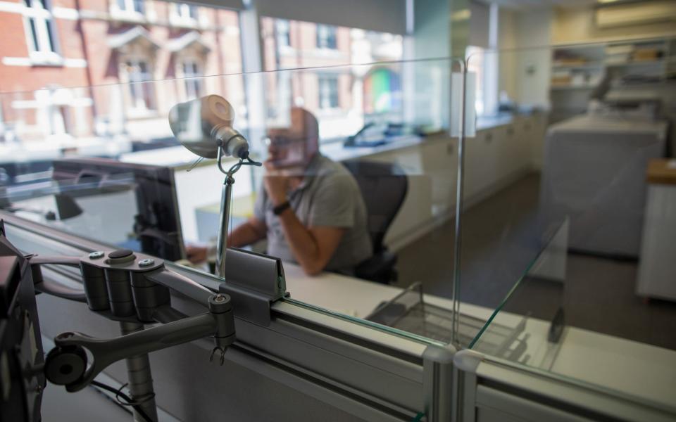 An employee is surrounded by protective screens at a workstation at offices in London - Chris Ratcliffe /Bloomberg 