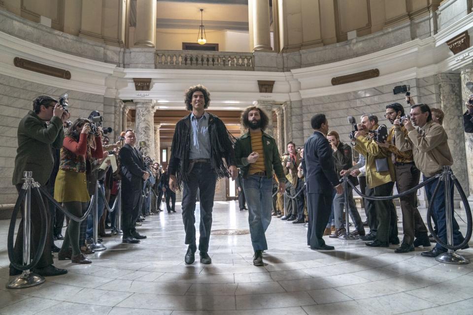 Two hippies walk between lines of reporters in the rotunda of a building