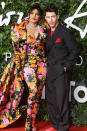 <p>coordinate as a couple in a vibrant floral Richard Quinn ensemble featuring a matching statement coat, bustier, trousers, boots and gloves (on her) and a black double-breasted suit with red sneakers (on him).</p>