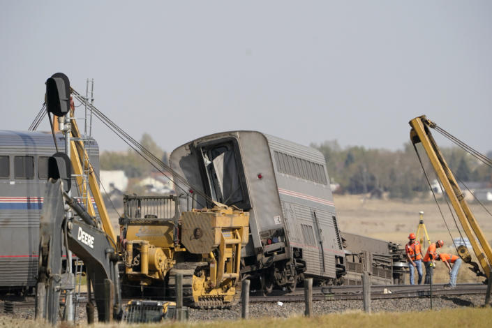 Workers examine a section of railroad track, Sunday, Sept. 26, 2021, next to cars from an Amtrak train that derailed the day before just west of Joplin, Mont., killing three people and injuring others. The westbound Empire Builder was en route to Seattle from Chicago, with two locomotives and 10 cars. (AP Photo/Ted S. Warren)