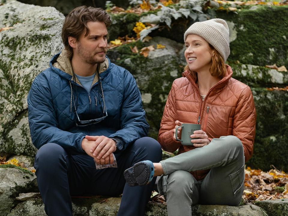 Luke Grimes as Jake and Ellie Kemper as Helen sitting on rocks in a scene from happiness for beginners