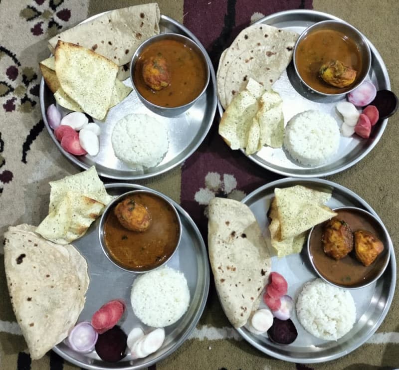 egg curry served with rice and a colourful assortment of carrot, beetroot, onions, and radish slices with papad accompaniment