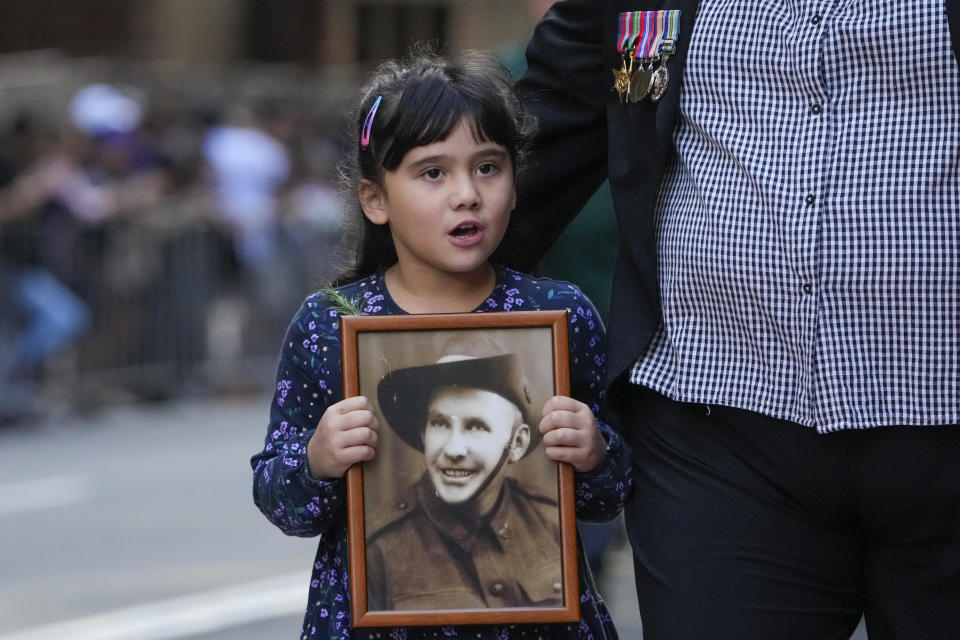 A young girl holds a photo as she marches during the Anzac Day parade in central the business district of Sydney, Australia, Thursday, April 25, 2024. (AP Photo/Mark Baker)