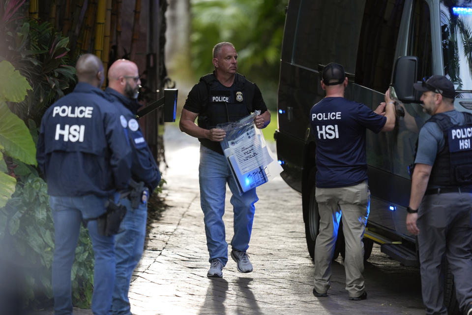 A law enforcement officer carries a bag of evidence to a pickup truck as federal agents stand at the entrance to a property belonging to rapper Sean Combs. 