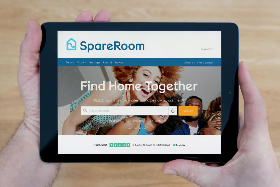 A man looks at the SpareRoom website on his iPad tablet device, shot against a wooden table top background (Editorial use only)
