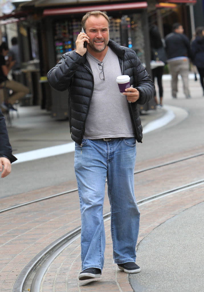 David DeLuise walking outside, talking on the phone, and holding a coffee cup