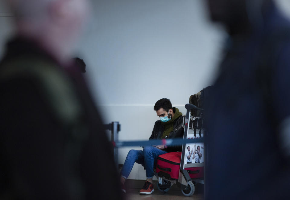A man wears a protective mask as he sits on his luggage in the main terminal of Brussels International Airport in Brussels, Friday, March 13, 2020. European Union interior ministers on Friday were trying to coordinate their response to the COVID-19 coronavirus as the number of cases spreads throughout the 27-nation bloc and countries take individual measures to slow the disease down. For most people, the new coronavirus causes only mild or moderate symptoms, such as fever and cough. For some, especially older adults and people with existing health problems, it can cause more severe illness, including pneumonia. (AP Photo/Virginia Mayo)